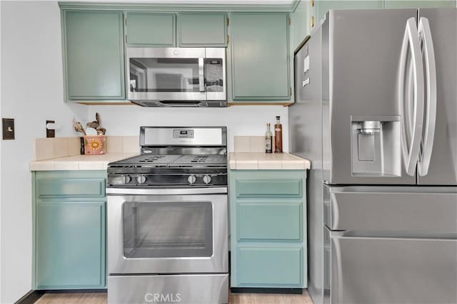 kitchen with tile countertops, light wood-type flooring, and appliances with stainless steel finishes