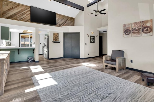 living area featuring a ceiling fan, beamed ceiling, wood finished floors, and baseboards