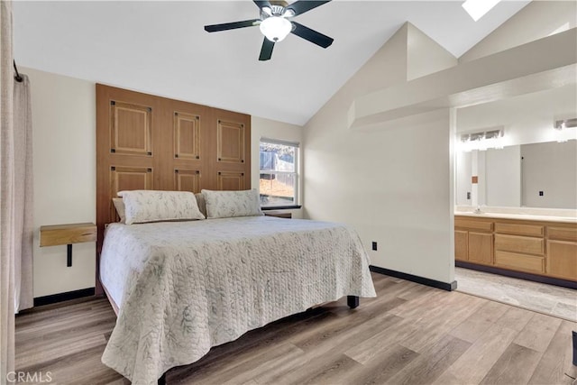 bedroom with baseboards, light wood finished floors, ceiling fan, vaulted ceiling, and connected bathroom