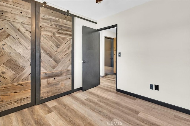 unfurnished room with a barn door, baseboards, and wood finished floors