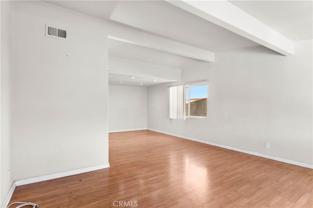 spare room featuring lofted ceiling with beams, wood finished floors, visible vents, and baseboards