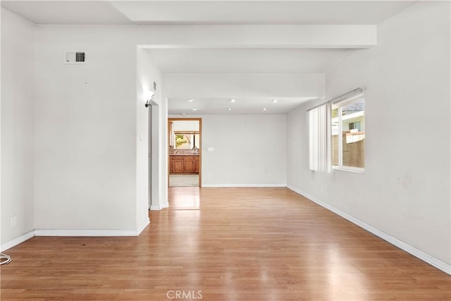 empty room featuring light wood-type flooring, baseboards, beamed ceiling, and visible vents