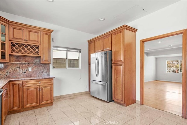 kitchen with backsplash, baseboards, light stone counters, freestanding refrigerator, and brown cabinetry
