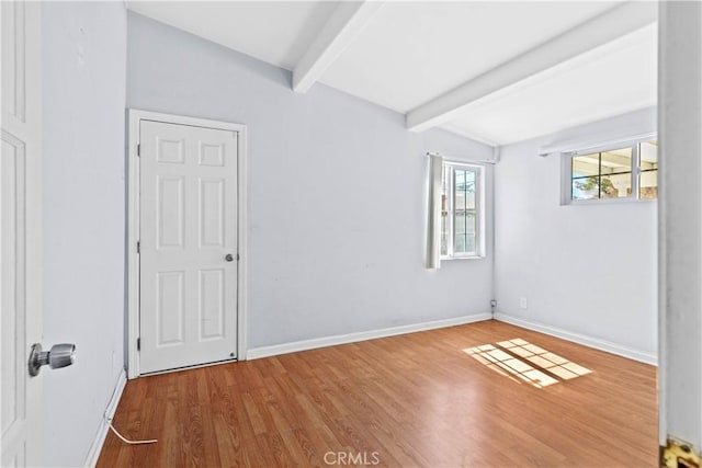 spare room with beam ceiling, wood finished floors, and baseboards
