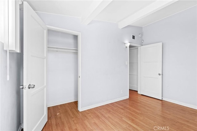 unfurnished bedroom featuring baseboards, beam ceiling, light wood-style floors, and visible vents