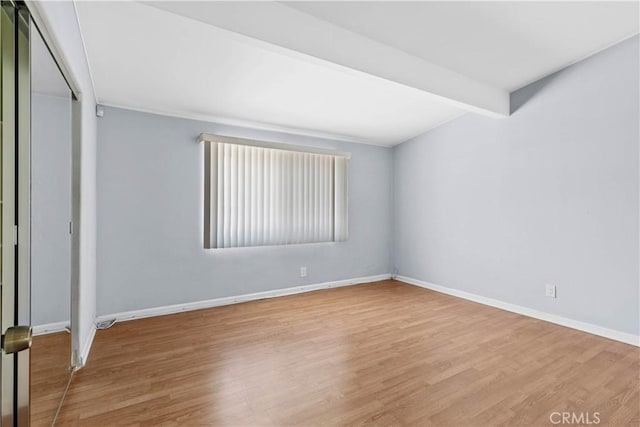 unfurnished bedroom with beamed ceiling, baseboards, a closet, and wood finished floors