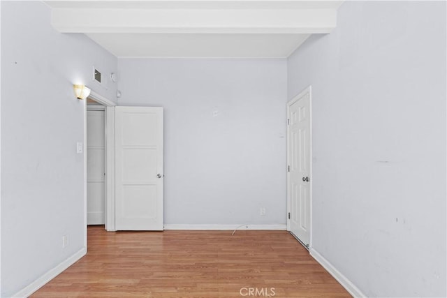 unfurnished room featuring beamed ceiling, light wood-type flooring, and baseboards