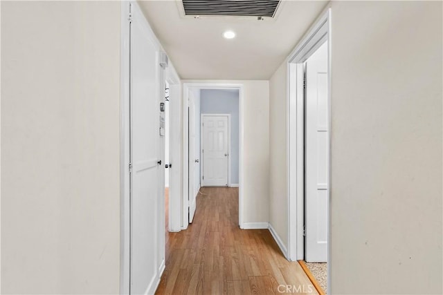 hallway with light wood-style flooring, baseboards, and visible vents
