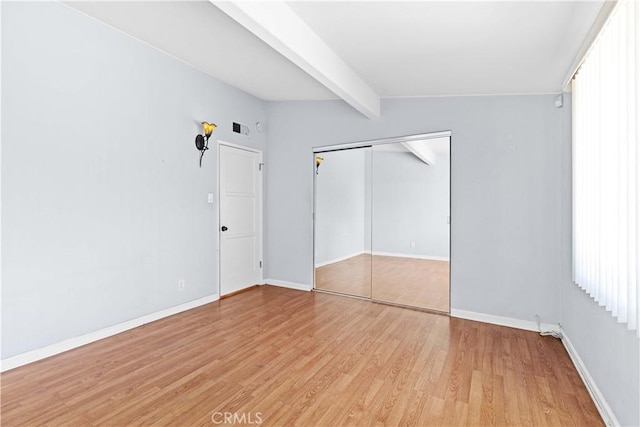 unfurnished bedroom featuring visible vents, baseboards, lofted ceiling with beams, light wood-style floors, and a closet