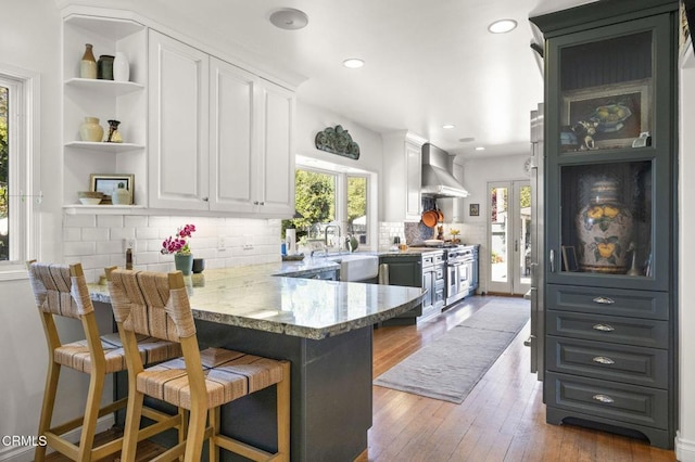 kitchen with light stone countertops, a healthy amount of sunlight, white cabinets, and wall chimney range hood