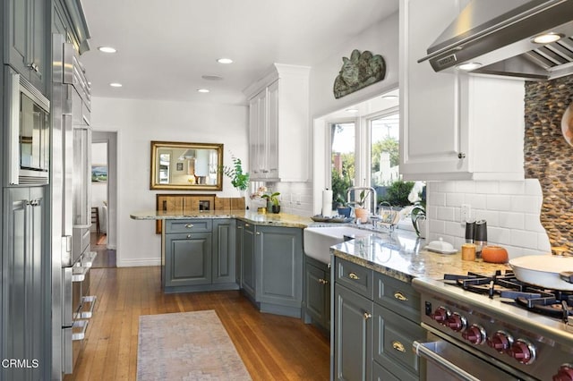 kitchen featuring wall chimney range hood, high quality appliances, wood-type flooring, and a sink