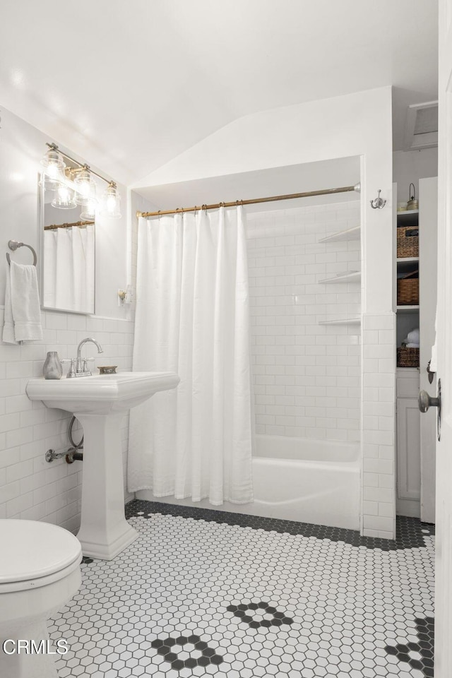 bathroom featuring lofted ceiling, shower / bath combo, a sink, tile walls, and toilet