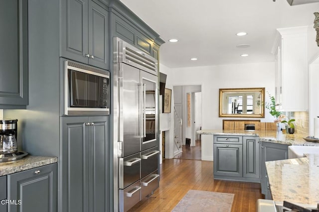 kitchen featuring a peninsula, recessed lighting, dark wood-style flooring, built in appliances, and tasteful backsplash