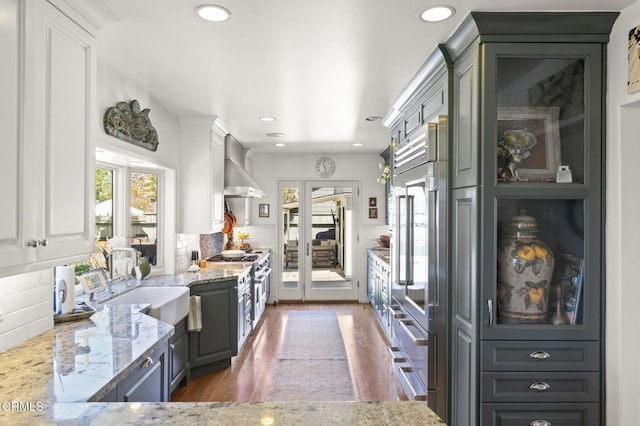 kitchen featuring wood finished floors, white cabinets, wall chimney range hood, decorative backsplash, and light stone countertops