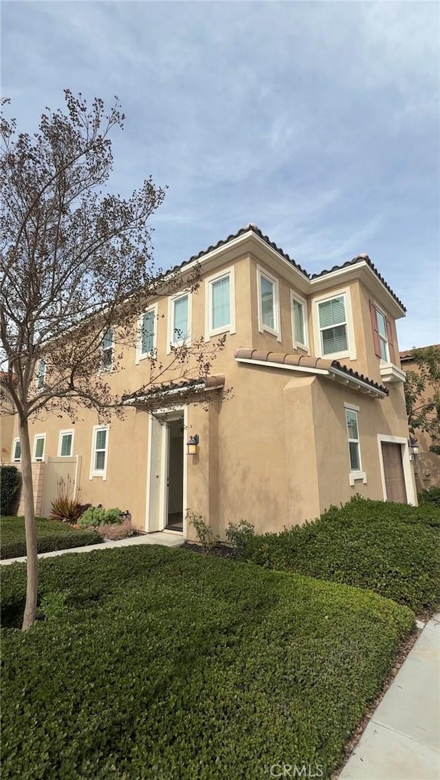 view of front of house featuring a front lawn, a tiled roof, an attached garage, and stucco siding