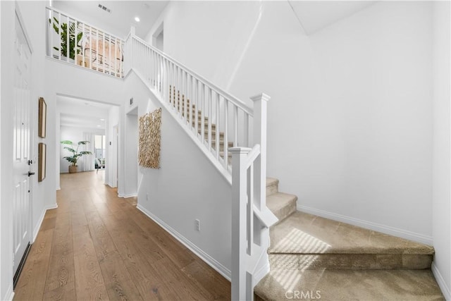 stairway with visible vents, wood finished floors, baseboards, and a towering ceiling