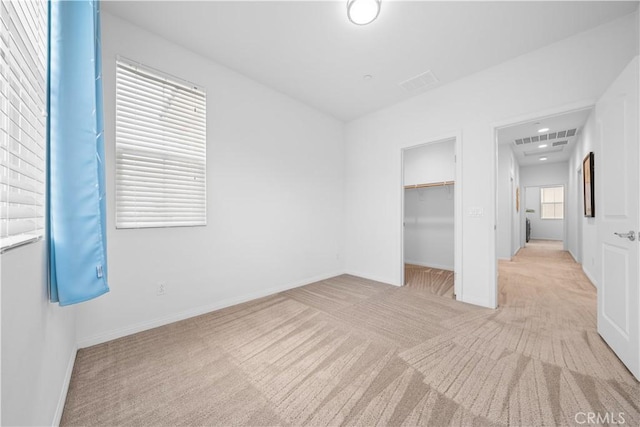 unfurnished bedroom with a walk in closet, baseboards, visible vents, and carpet floors