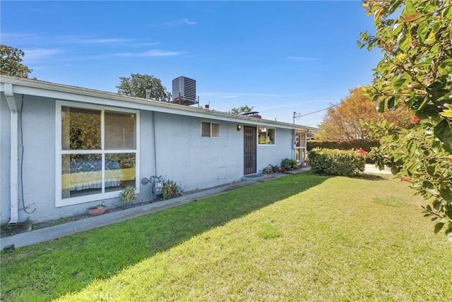 rear view of property with central air condition unit, stucco siding, and a yard