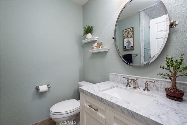 bathroom with tasteful backsplash, toilet, vanity, and a textured wall