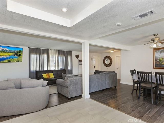 living room with a textured ceiling, a ceiling fan, visible vents, and wood finish floors