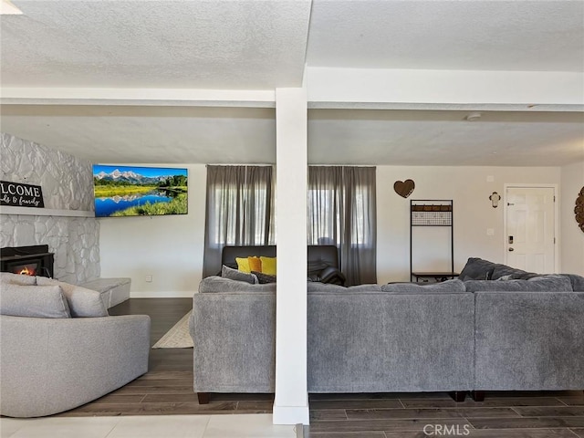 living area featuring a stone fireplace, a textured ceiling, baseboards, and wood tiled floor