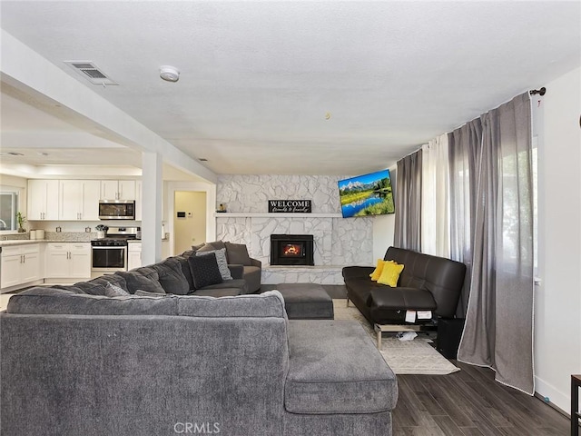 living area with dark wood finished floors, visible vents, and a stone fireplace