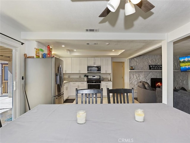 dining area featuring visible vents, ceiling fan, a fireplace, and a tray ceiling