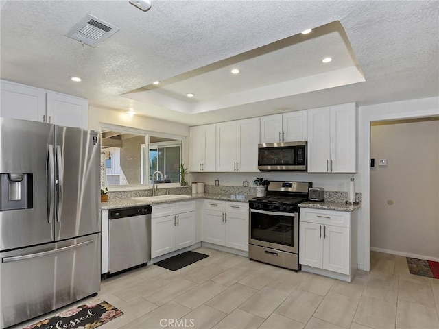 kitchen featuring visible vents, appliances with stainless steel finishes, white cabinetry, and a raised ceiling