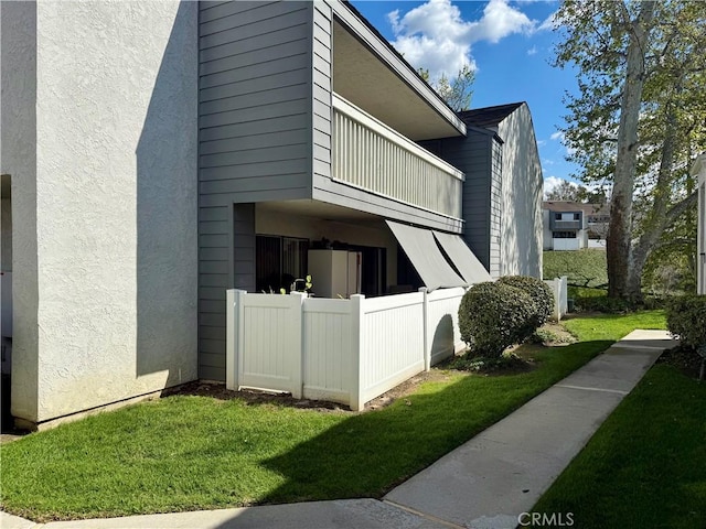 view of side of home with stucco siding, a lawn, a balcony, and fence