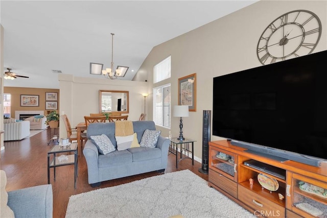 living area with visible vents, lofted ceiling, ceiling fan with notable chandelier, a tile fireplace, and wood finished floors