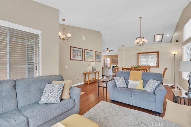 living room featuring wood finished floors, visible vents, baseboards, lofted ceiling, and ceiling fan with notable chandelier