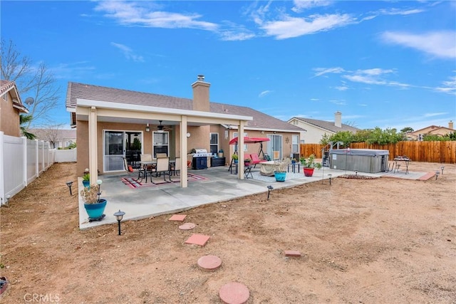 rear view of property featuring a hot tub, stucco siding, a chimney, a fenced backyard, and a patio