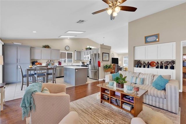 living room featuring visible vents, light wood-style flooring, a ceiling fan, and lofted ceiling