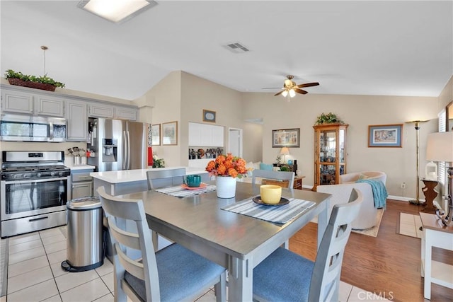 dining area with baseboards, visible vents, light tile patterned flooring, ceiling fan, and vaulted ceiling