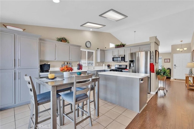 kitchen with a kitchen island, lofted ceiling, a sink, light countertops, and appliances with stainless steel finishes