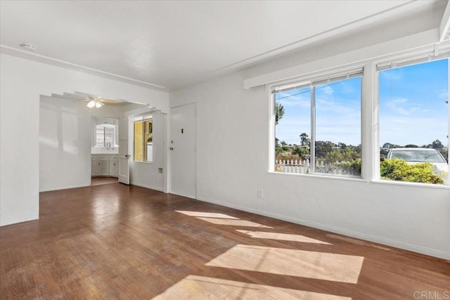 unfurnished living room featuring arched walkways, ceiling fan, baseboards, and wood finished floors