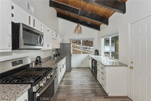 kitchen with lofted ceiling with beams, dark wood-style floors, stainless steel appliances, wooden ceiling, and light stone countertops