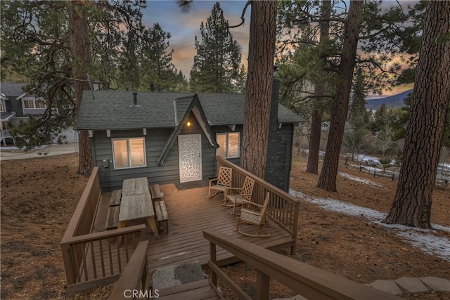 back of property at dusk featuring a wooden deck and a shingled roof