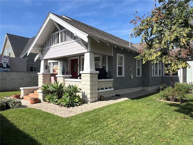 view of side of home featuring a porch, a lawn, and roof with shingles