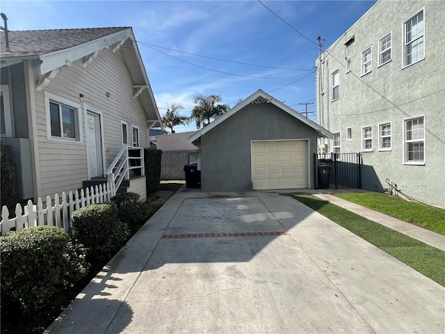 view of side of home featuring stucco siding, driveway, fence, an outdoor structure, and a garage