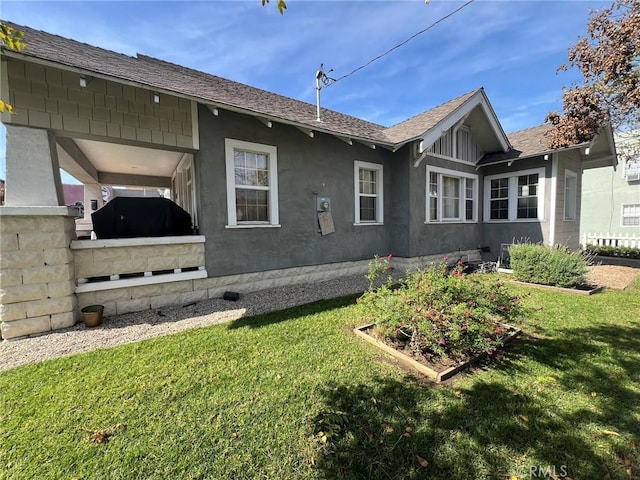 back of property featuring a yard, stucco siding, and a shingled roof