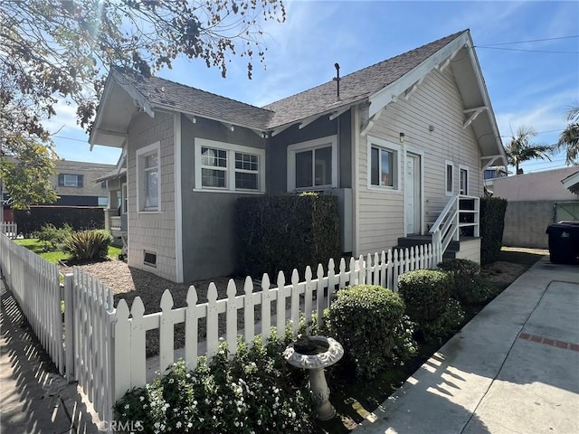 view of property exterior with a fenced front yard and a shingled roof