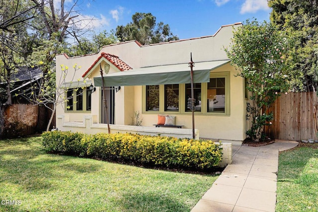 view of front of house featuring stucco siding, a front yard, and fence