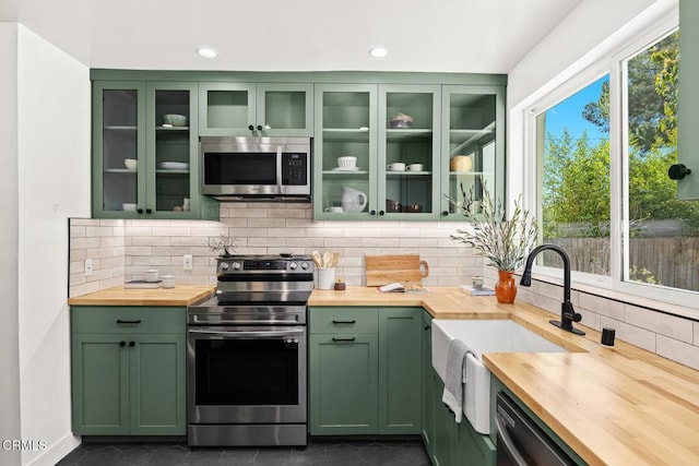 kitchen featuring green cabinetry, decorative backsplash, appliances with stainless steel finishes, and butcher block counters