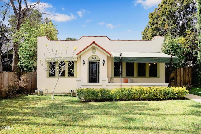 view of front of house with a front yard, fence, a tile roof, and stucco siding