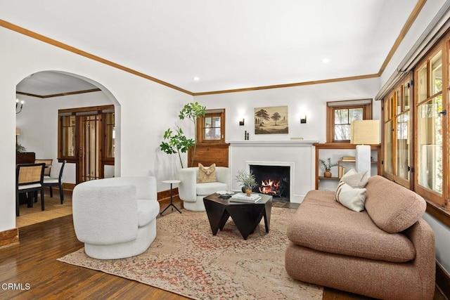 living room featuring arched walkways, a fireplace with flush hearth, ornamental molding, and wood finished floors