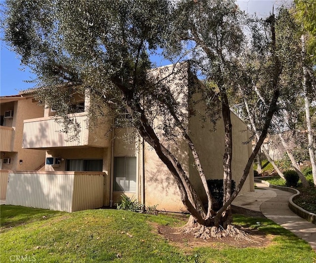 view of home's exterior with stucco siding, a lawn, a balcony, and fence