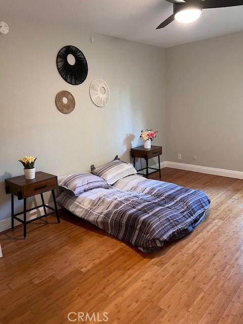 bedroom featuring baseboards, wood finished floors, and a ceiling fan