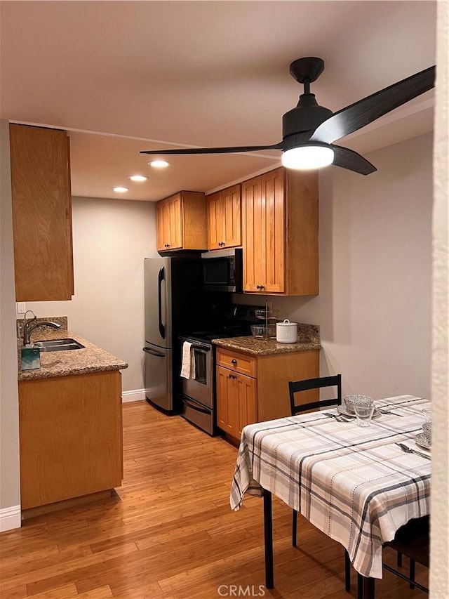 kitchen with a ceiling fan, baseboards, light wood finished floors, a sink, and appliances with stainless steel finishes