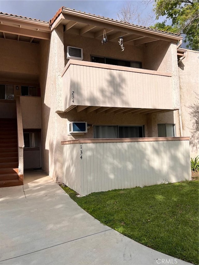 view of side of property with stucco siding, a balcony, a lawn, and a tile roof